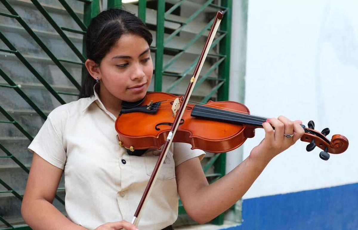 Luisa, víctima del acoso de las bandas en Honduras, toca el violín en su escuela, a través de la lectura, la escritura y la música muestra su lado creativo y su capacidad para encontrar la alegría en diversas formas de expresión personal.
